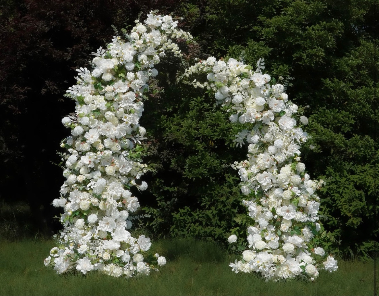 White floral arch set on green grass for an outdoor celebration