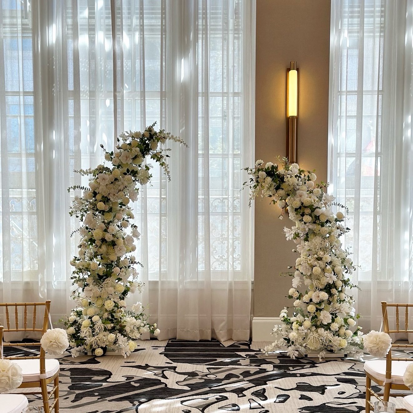 White floral arch pair arranged in front of tall ballroom windows