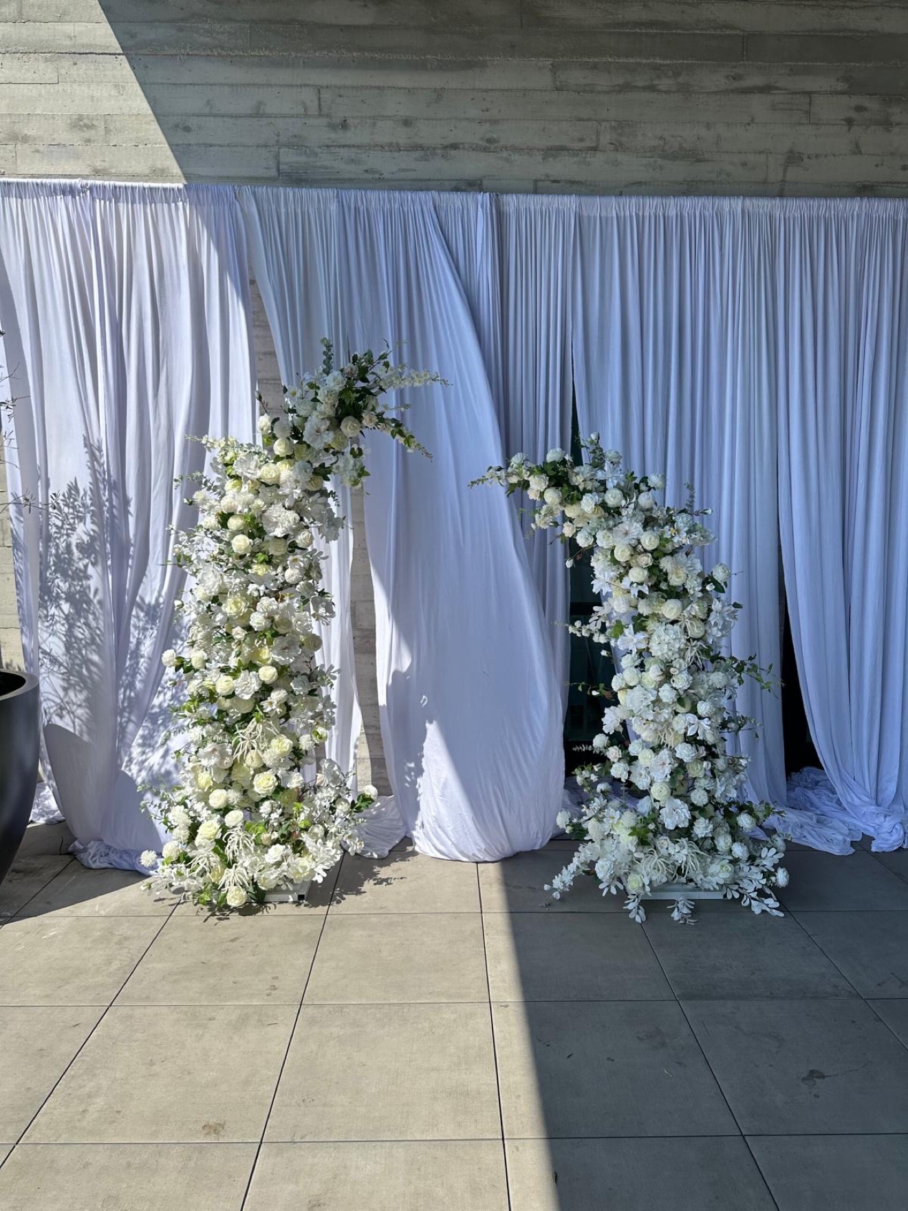 White floral arch pair beneath a draped outdoor canopy