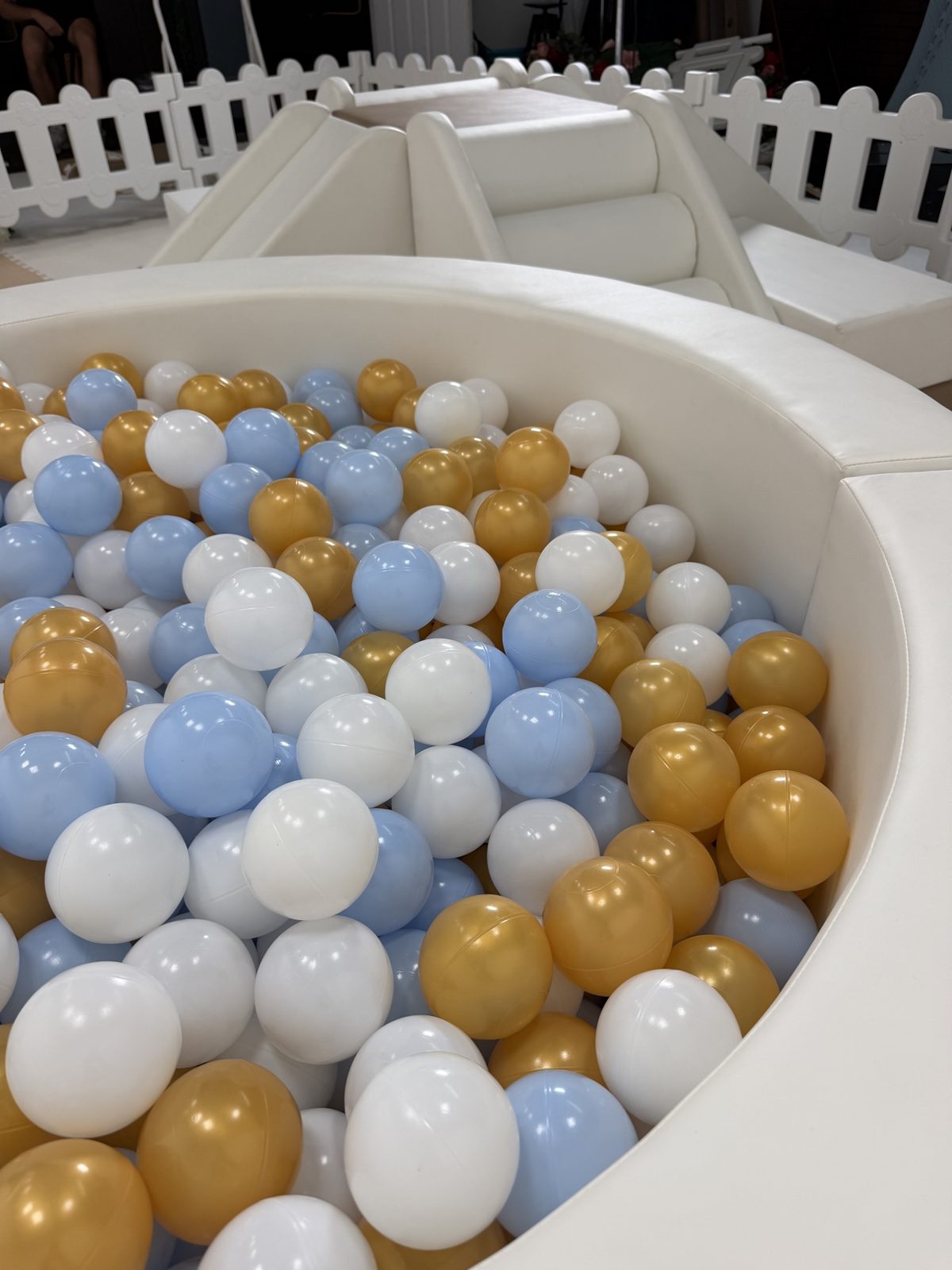 Close view into the soft-play ball pit with white, blue and gold balls